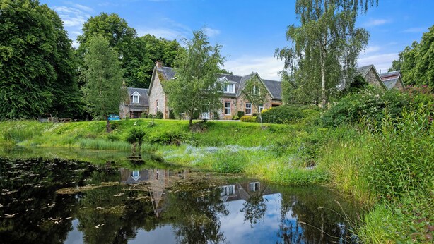 Een huis met een vijver ervoor, omringd door groen en bomen.