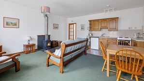Een gezellige woonkamer met een bank, houten stoelen, een eettafel en een open haard.