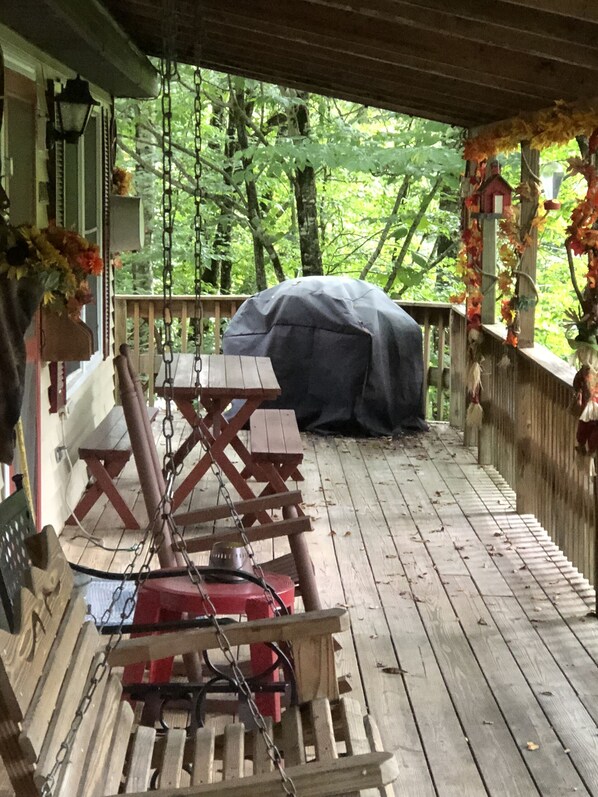 Una terraza de madera con mesas de picnic y una parrilla.