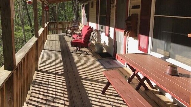 A covered porch with wooden railings, a red bench, a picnic table, and a view of the forest.