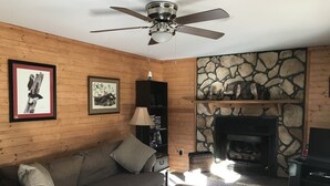 A cozy living room with a stone fireplace, a ceiling fan, and a sofa.