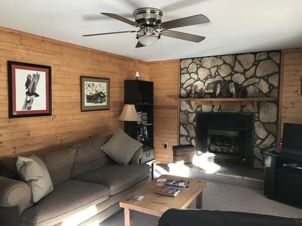A cozy living room with a stone fireplace, a ceiling fan, and a sofa.