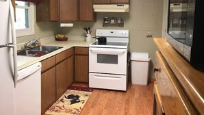 A compact kitchen with wooden cabinets, a white stove, a microwave, and a small refrigerator.
