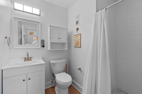 A bathroom with a white sink, toilet, and shower curtain. - A Beach Odyssea at Admirals View III 2 Bedroom Oceanfront Condo, Pool Access, Near Kill Devil Hills Attractions (Kill Devil Hills)