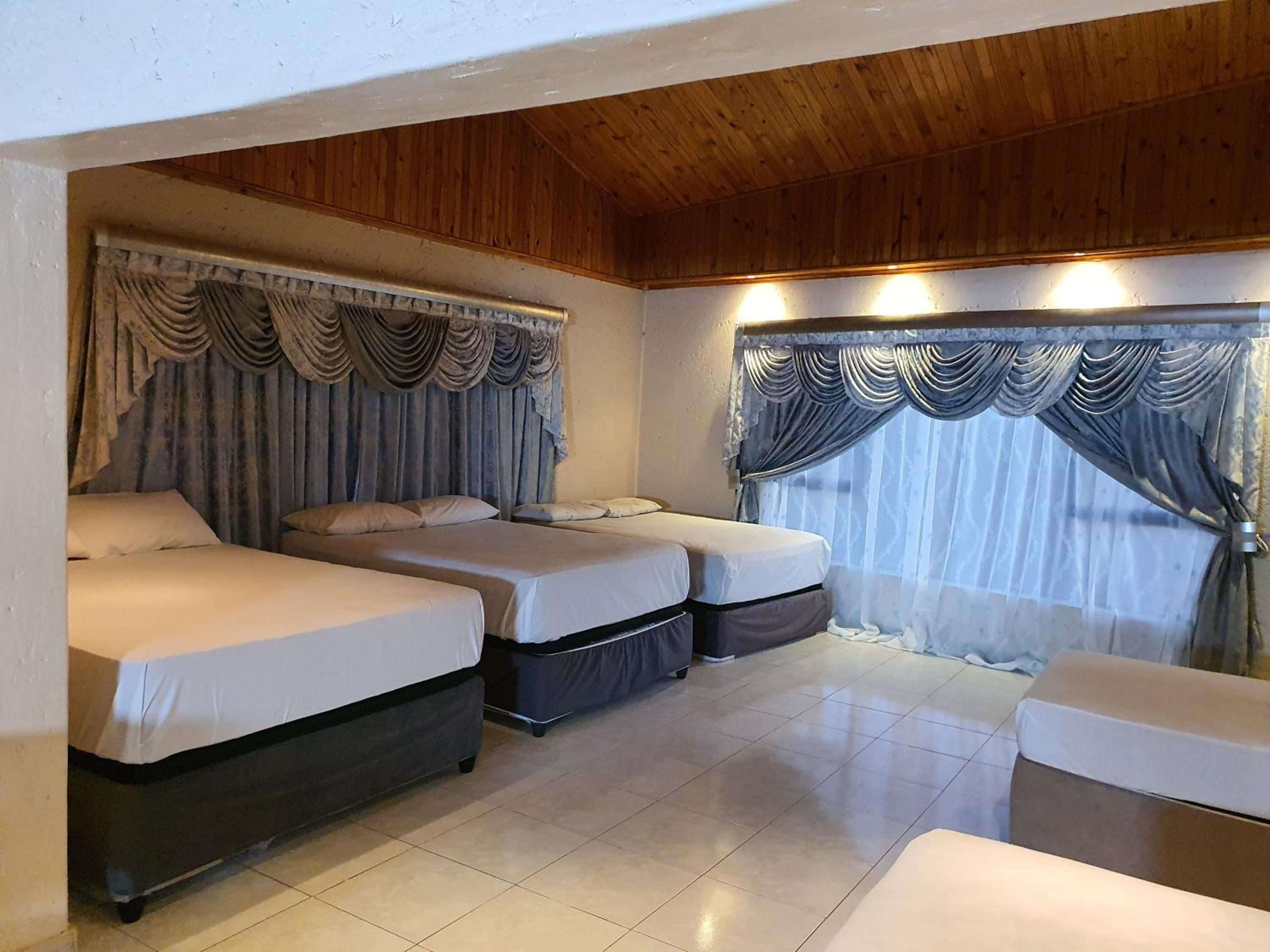 Een kamer met twee bedden, een bank, houten plafond en gordijnen.