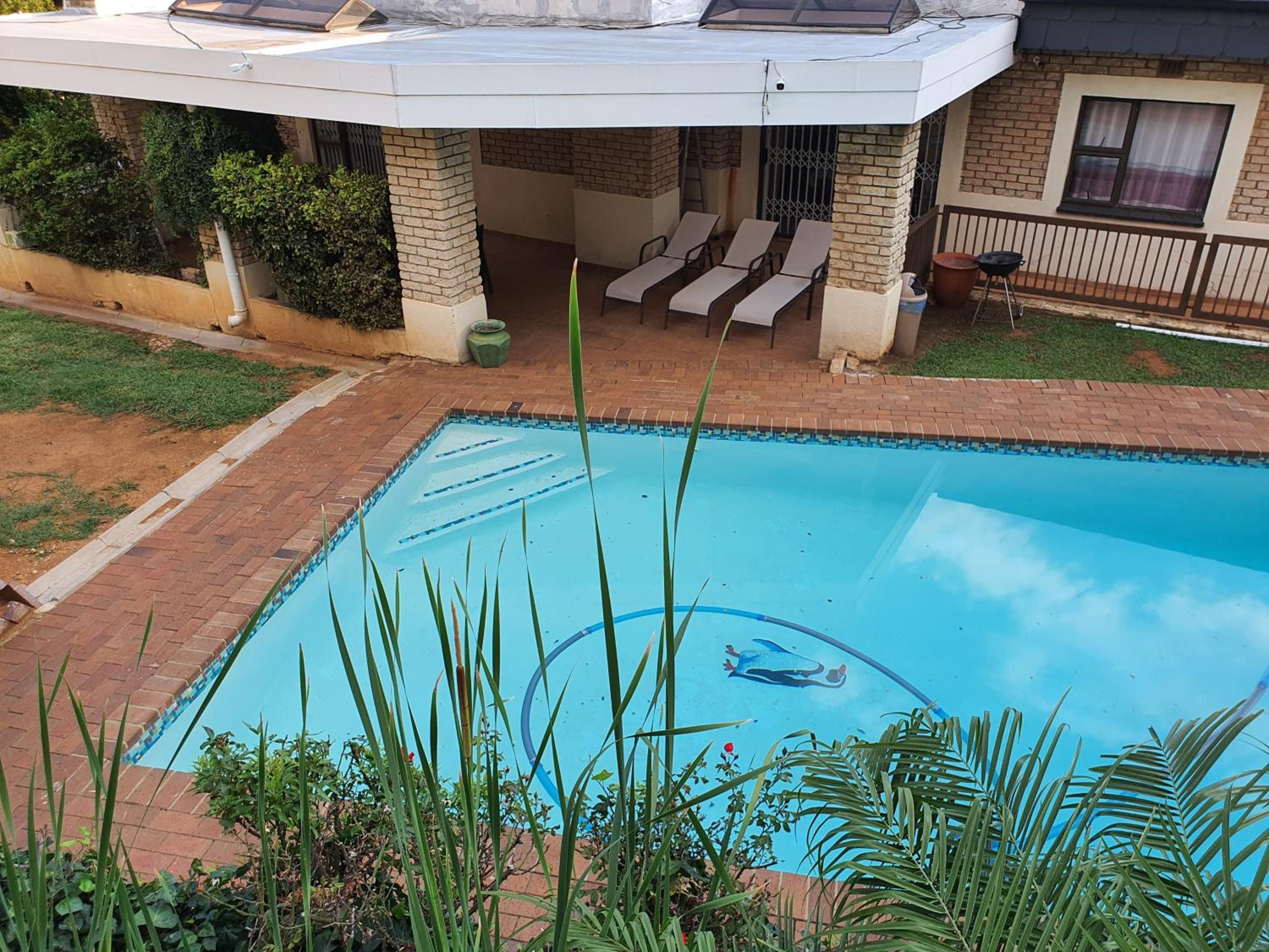 A swimming pool with a clear blue water feature, surrounded by a brick patio and a covered seating area with lounge chairs.