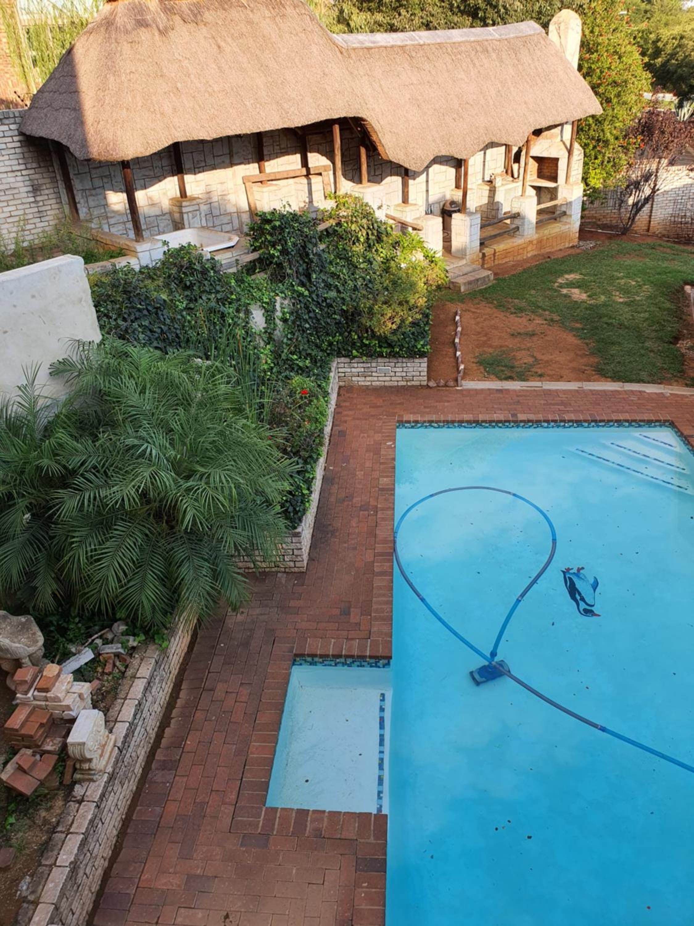 A swimming pool with a hose, surrounded by a brick patio and a thatched-roof structure.