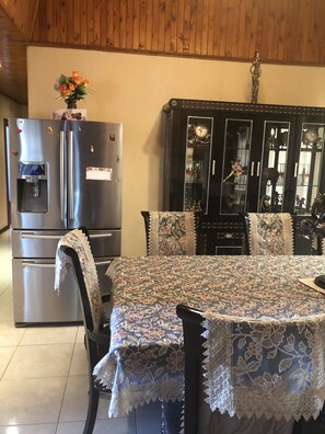 A dining area with a table covered in lace, a refrigerator, and a cabinet with glass doors. - Naomi's Place (Johannesburg South)