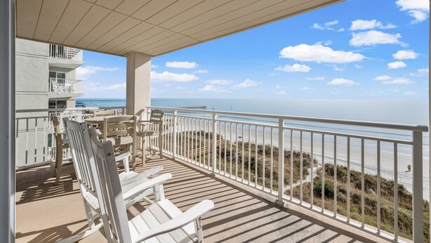 A balcony with white chairs and a view of the beach and ocean.