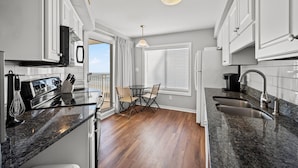 A modern kitchen with granite countertops, white cabinetry, a dining area with a table and chairs, and a view of the outdoors through a window.