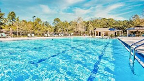 A swimming pool with clear blue water, surrounded by a fence, and a pavilion in the background.