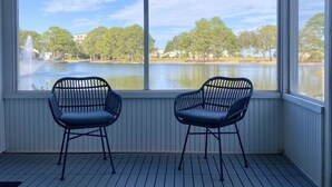 A covered outdoor area with two chairs facing a lake, wooden deck, and a view of trees and buildings.