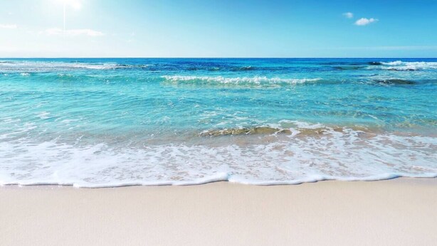 A beach with clear blue water and a sandy shore.