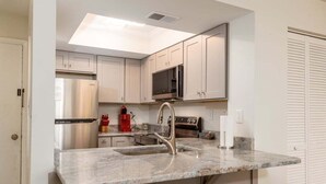 A modern kitchen with white cabinets, stainless steel appliances, a granite countertop, and a black upholstered stool. - Near beach indoor pool hot tub and outdoor pool (Myrtle Beach)