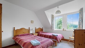 A bedroom with two beds, a wooden dresser, a window with a view of greenery, and a ceiling light fixture. - Aigas holiday cottages Pond View (By Beauly,, Inverness-shire)