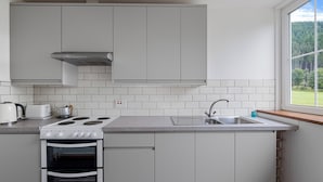 A modern kitchen with white cabinets, a built-in oven, a stove, and a window with a view of a forest. - Aigas holiday cottages Pond View (By Beauly,, Inverness-shire)