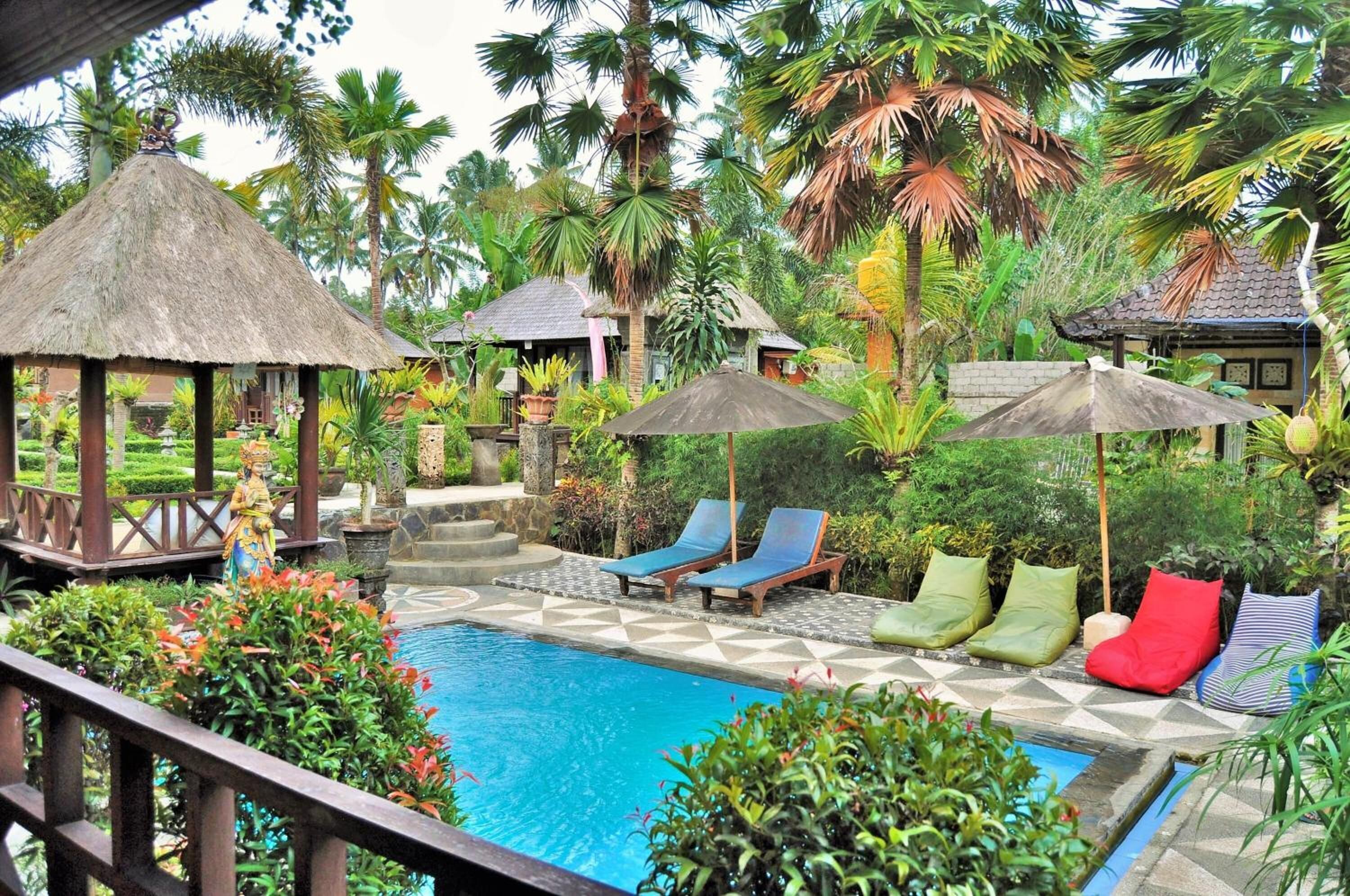 A pool area with lounge chairs and umbrellas, surrounded by lush tropical vegetation.