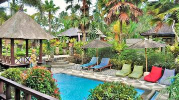A pool area with lounge chairs and umbrellas, surrounded by lush tropical vegetation.