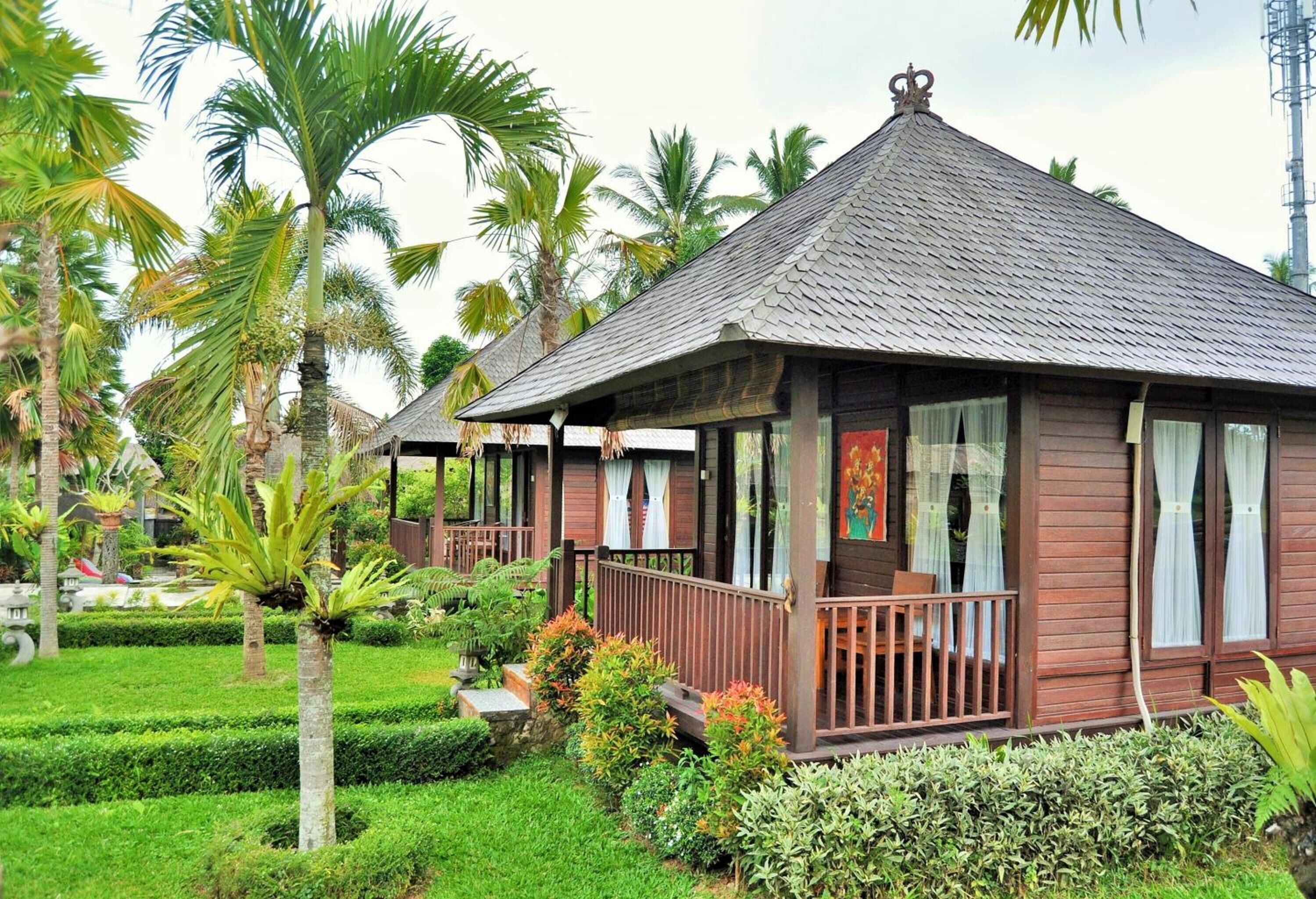A traditional wooden building with a tiled roof, surrounded by well-maintained tropical gardens and palm trees.