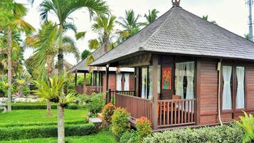 A traditional wooden building with a tiled roof, surrounded by well-maintained tropical gardens and palm trees.