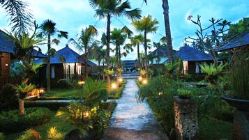 A pathway flanked by palm trees and illuminated by lights, leading to a building with a tiled roof.