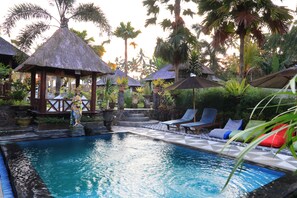 A pool area with lounge chairs, a thatched-roof gazebo, and tropical plants. - Uma Dong Loka Village (Abiansemal)