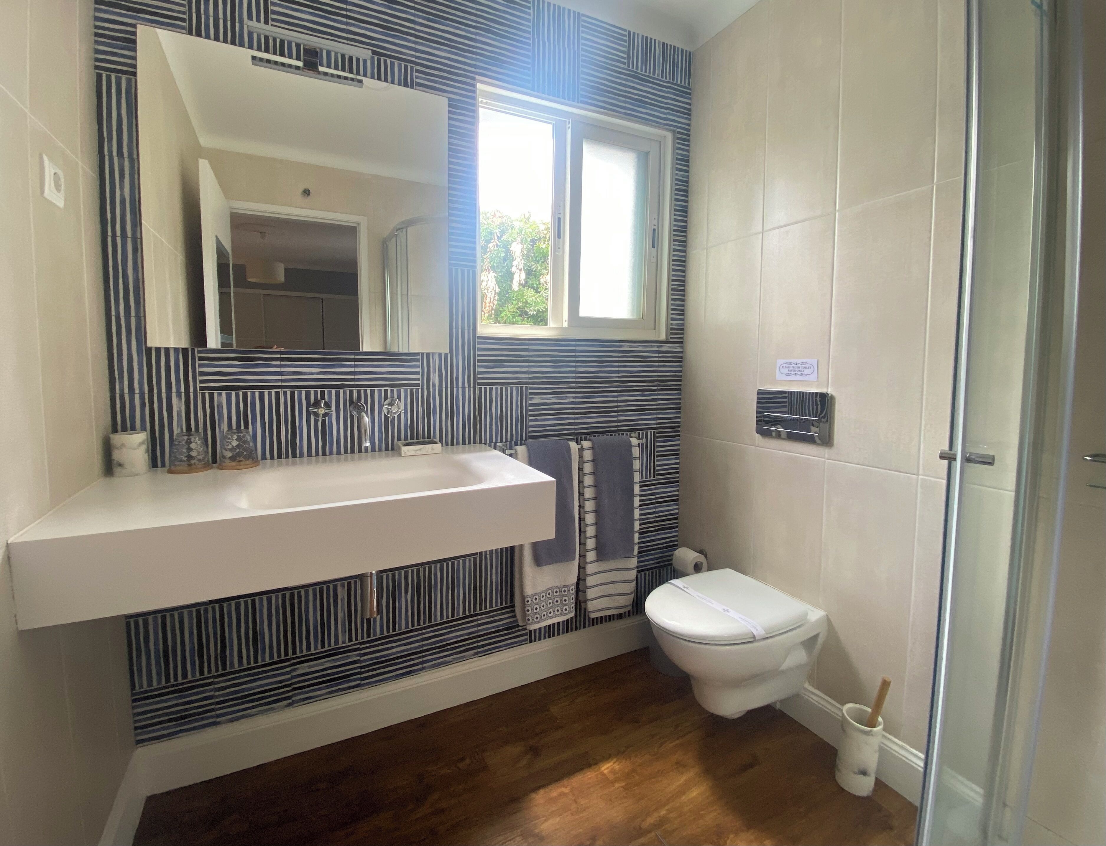 Un bagno con lavandino bianco, uno specchio, parete a righe, un water e zona doccia.