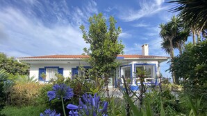 A house with a red-tiled roof, surrounded by lush greenery and blue flowers. - Quinta dos Bravos (Ribeira Grande)