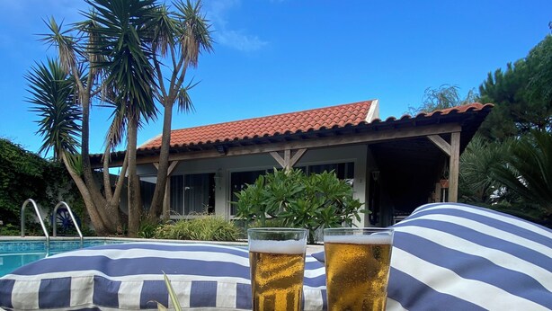 A poolside setting with two glasses of amber liquid, a bowl of assorted nuts and dried fruits, and striped pillows. - Quinta dos Bravos (Ribeira Grande)