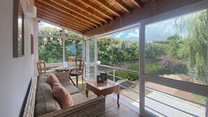 A modern living room with a wooden ceiling, large windows, a sofa, a dining table, and chairs. - Quinta dos Bravos (Ribeira Grande)