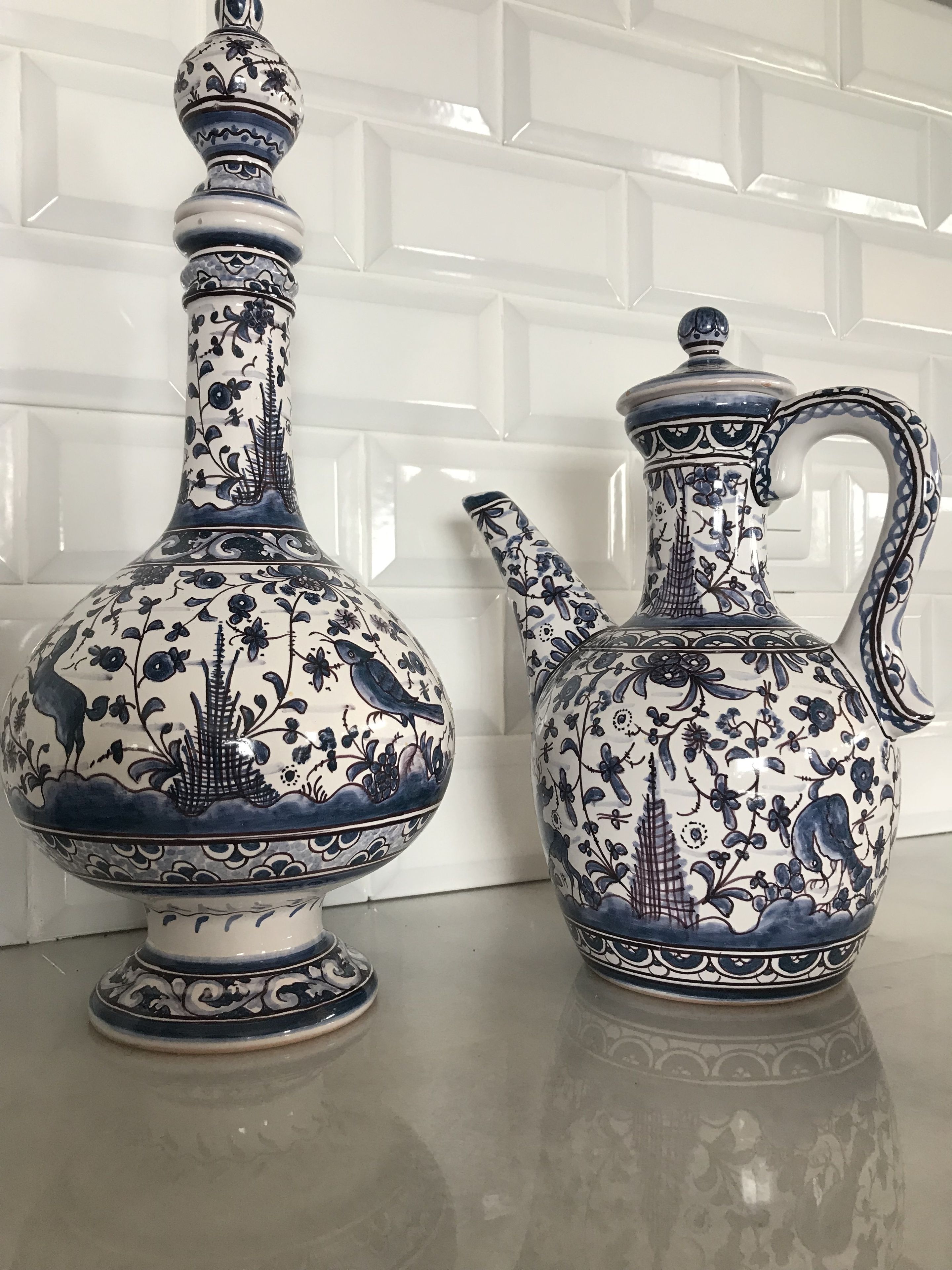 Dois vasos de cerâmica com motivos florais e de pássaros refletidos numa superfície.
