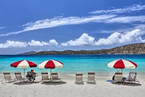 Una playa con tres sombrillas y cuatro sillas de playa.