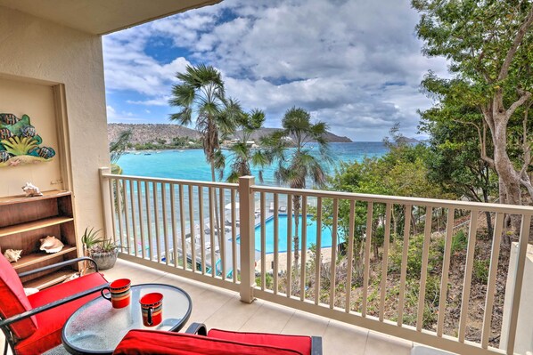Un balcón con vista a una piscina turquesa, sillas rojas y un paisaje tropical.