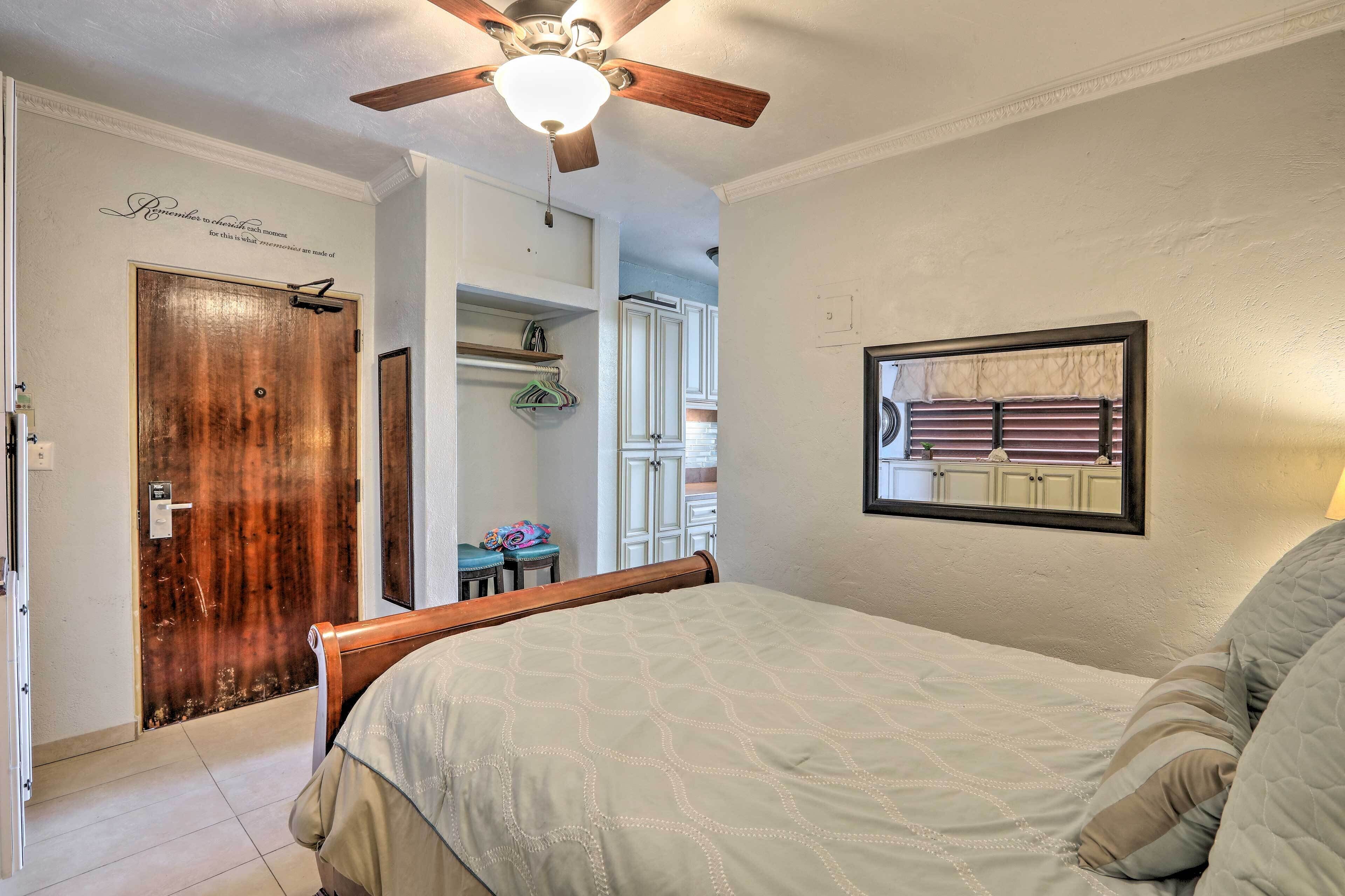 A bedroom with a bed, a ceiling fan, a wooden door, and a mirror on the wall.