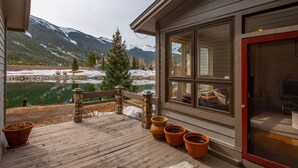Une terrasse en bois agrémentée de plantes en pot, une balustrade en pierre et une vue sur un lac et des montagnes.