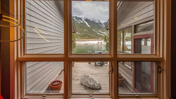 Une vue à travers une fenêtre à cadre en bois, donnant sur une montagne, une étendue d’eau et un quai avec un bateau.