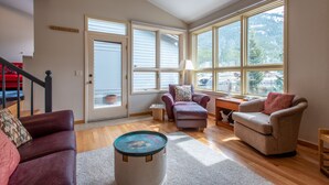 Un salon spacieux avec une grande fenêtre, un escalier rouge et un fauteuil beige.