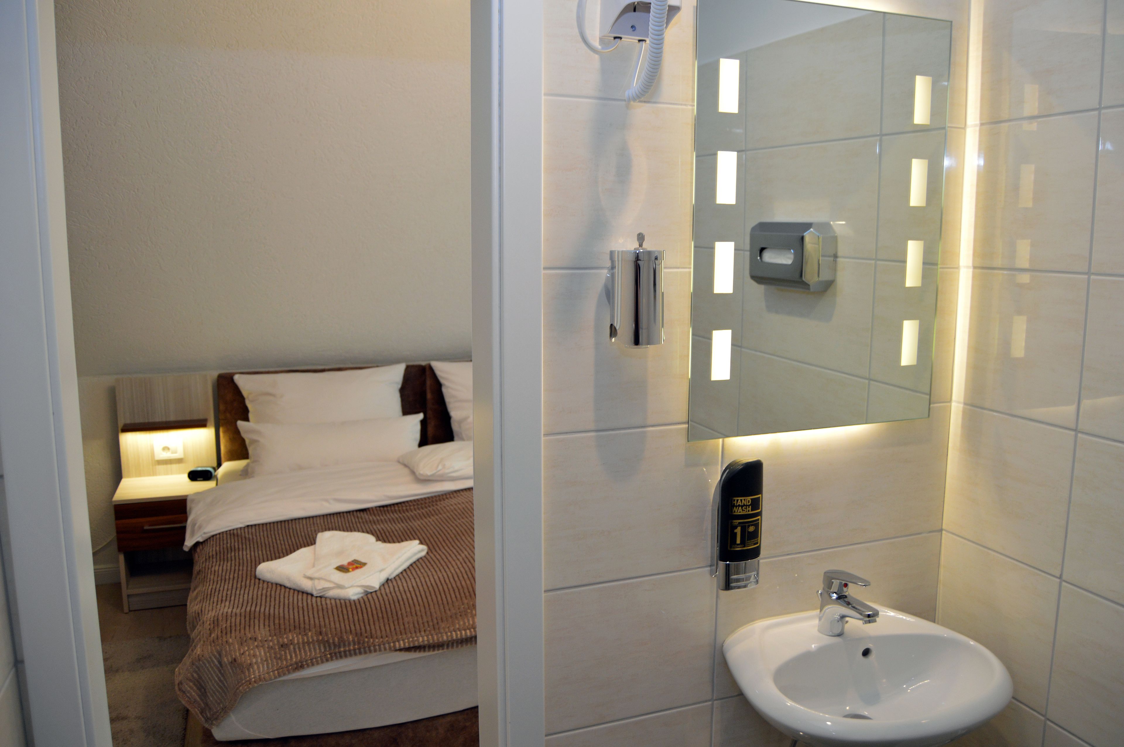 Ein Hotelzimmer mit Bett, Nachttisch und Badezimmer mit Waschbecken und Spiegel.