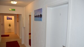 En hall med en röd matta, en målning som föreställer hus, en dörr med nummer 9, och ett litet bord med en växt.
