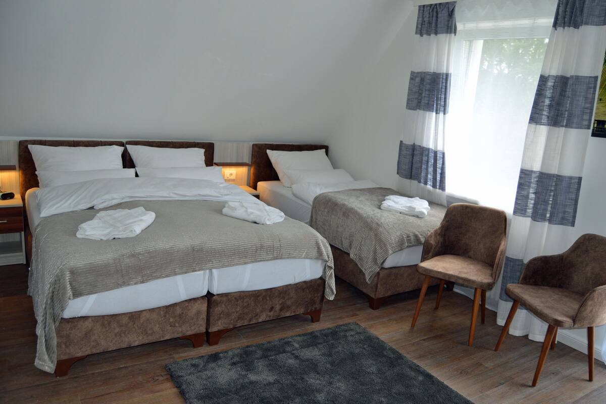 Habitación de hotel con dos camas, una silla y una mesita de noche con lámpara.