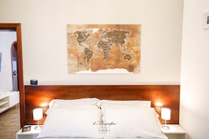 Quarto de hotel com cabeceira de madeira, cama com roupa de cama branca, duas luminárias de cabeceira e um mapa-múndi na parede.