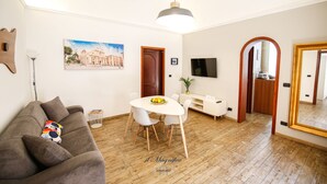A modern living room with a sofa, dining table, and chairs. There is a painting on the wall, a TV, and a large mirror. - The Magnificent Apartment (Catania)