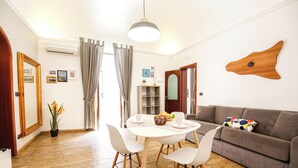 A modern living room with a wooden floor, white furniture, a grey sofa, and a unique wooden wall clock. - The Magnificent Apartment (Catania)