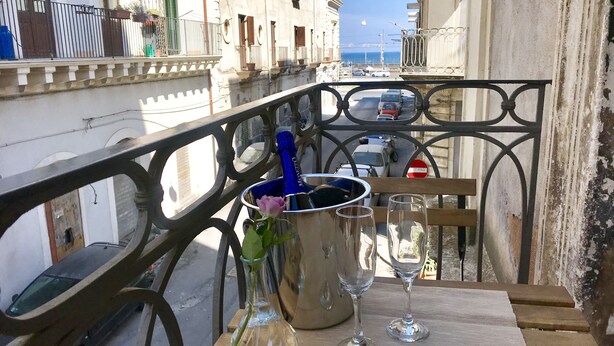 A balcony with a table set for two, a champagne bottle, and a vase with a single flower. - The Magnificent Apartment (Catania)