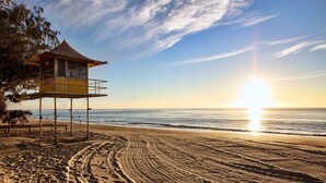 Una torretta di salvataggio su una spiaggia, con cieli sereni e il sole che tramonta sull'oceano.