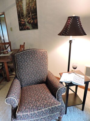 A patterned armchair, a table with a book and a glass of wine, and a floor lamp.