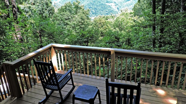 A wooden deck with two rocking chairs and a table, overlooking a forested valley.