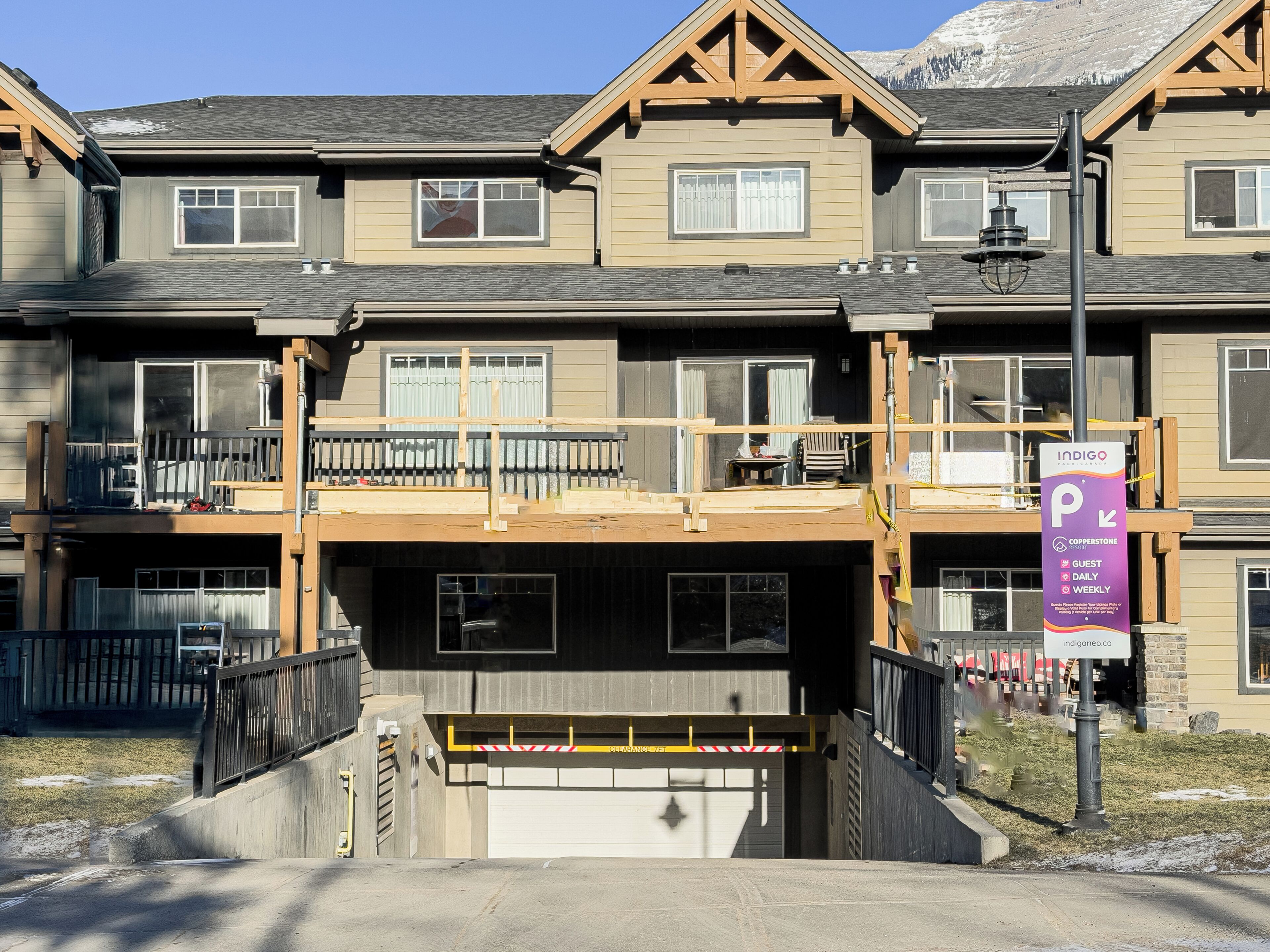 A multi-story building with a covered parking area, a guest sign, and a view of mountains.