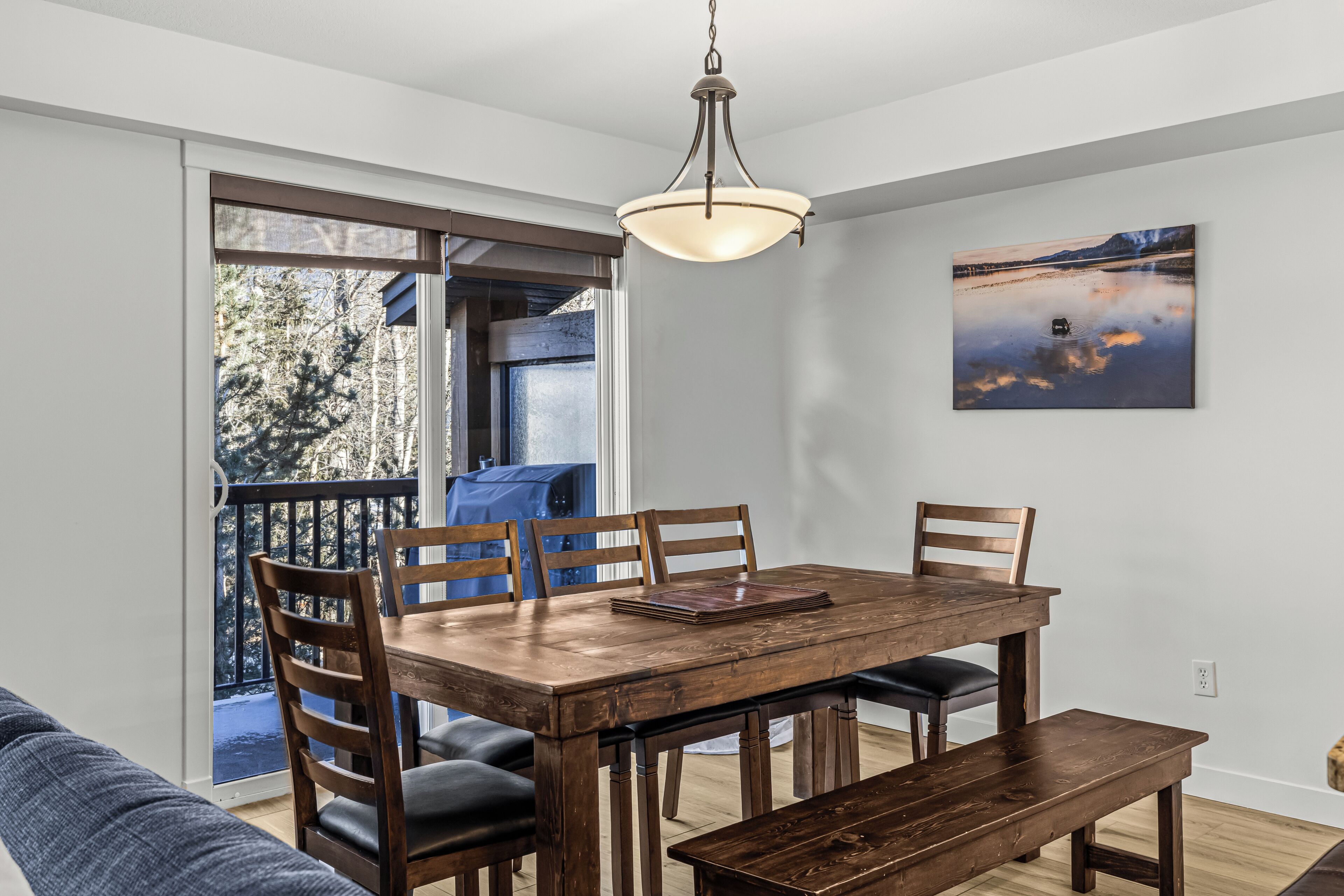 Een eetruimte met een houten tafel, stoelen, een bank en een plafondlamp.