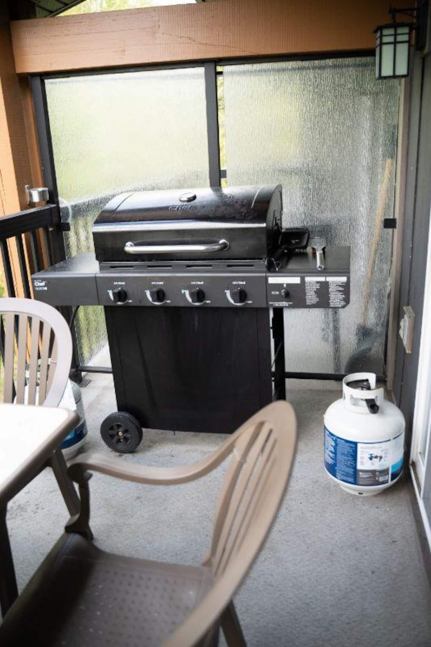 Grill med gasbeholder og stol foran.